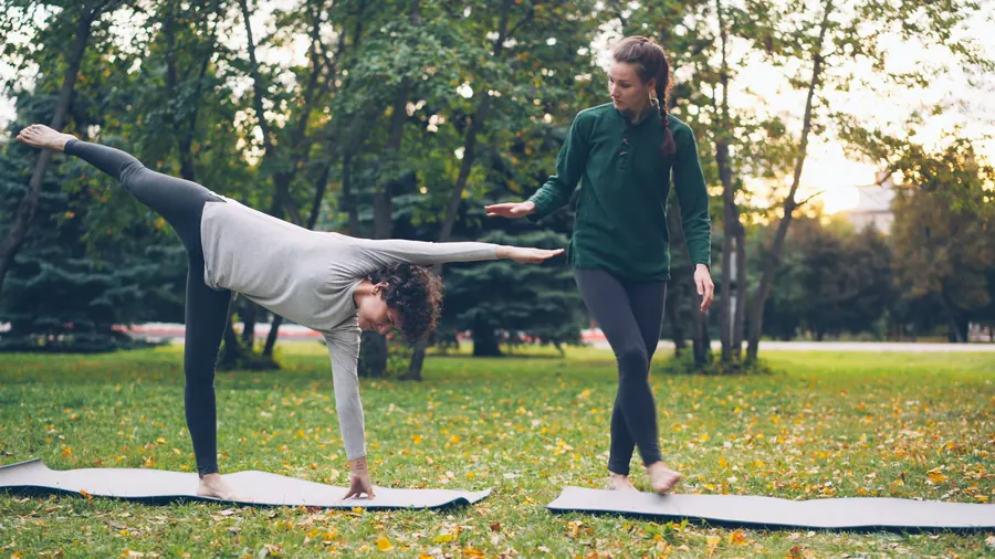 Coach qui aide une femme à tenir une posture d'équilibre dans un parc