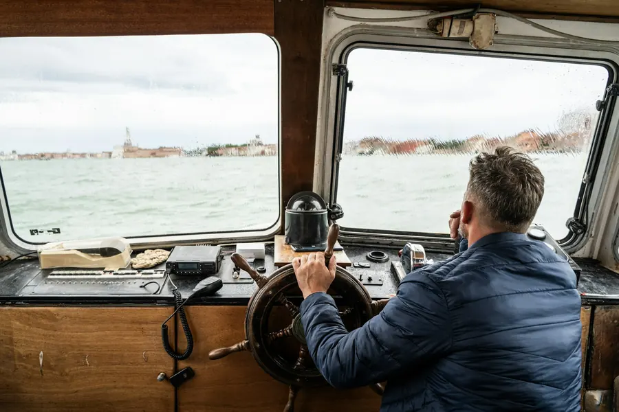 Homme au gouvernail d'un bateau, veste marine, mer en arrière-plan