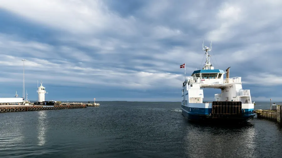 Bateau à passagers qui quitte le port devant la jetée et son phare
