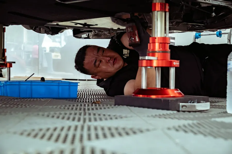 Mécanicien sous une voiture sur pont élévateur, atelier propre et bien éclairé