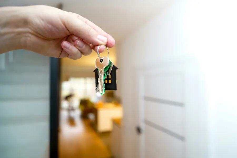 Main tenant une clé avec porte-clés maison devant une entrée