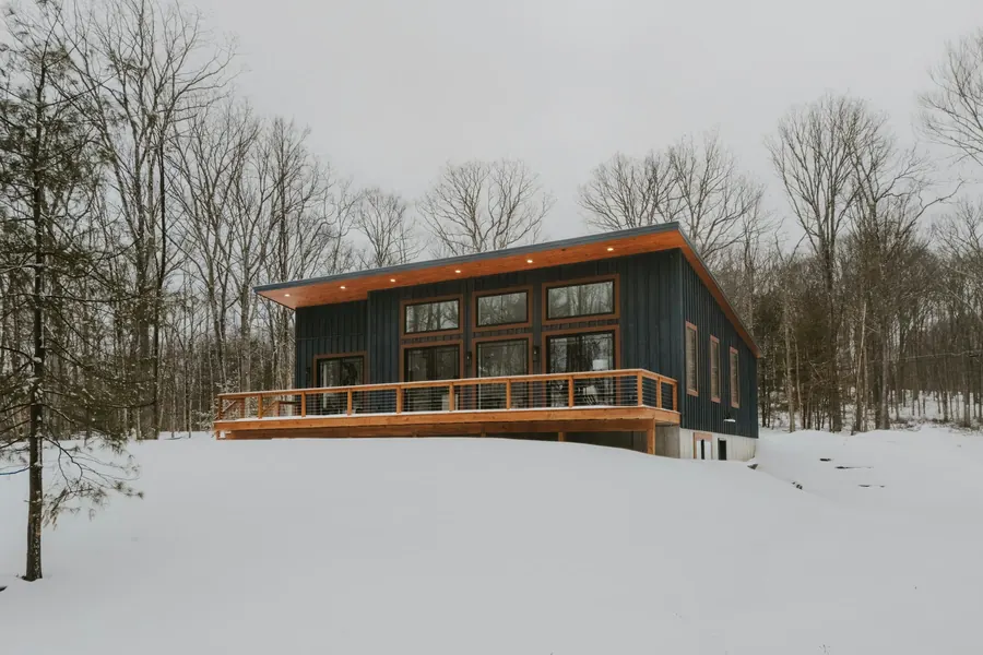 Maison contemporaine sur pilotis, terrasse en bois, forêt enneigée