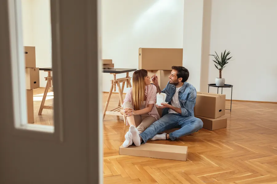 Couple de trentenaires assis au sol entre des cartons, séjour lumineux d'une maison ancienne, poutres