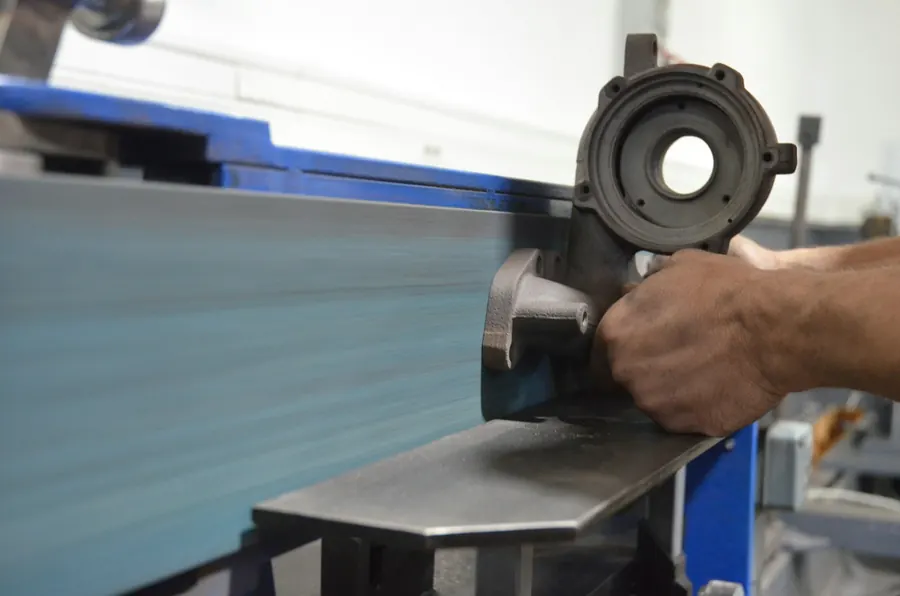 Zingueur qui plie une feuille de zinc dans un petit atelier, établi et chutes de métal