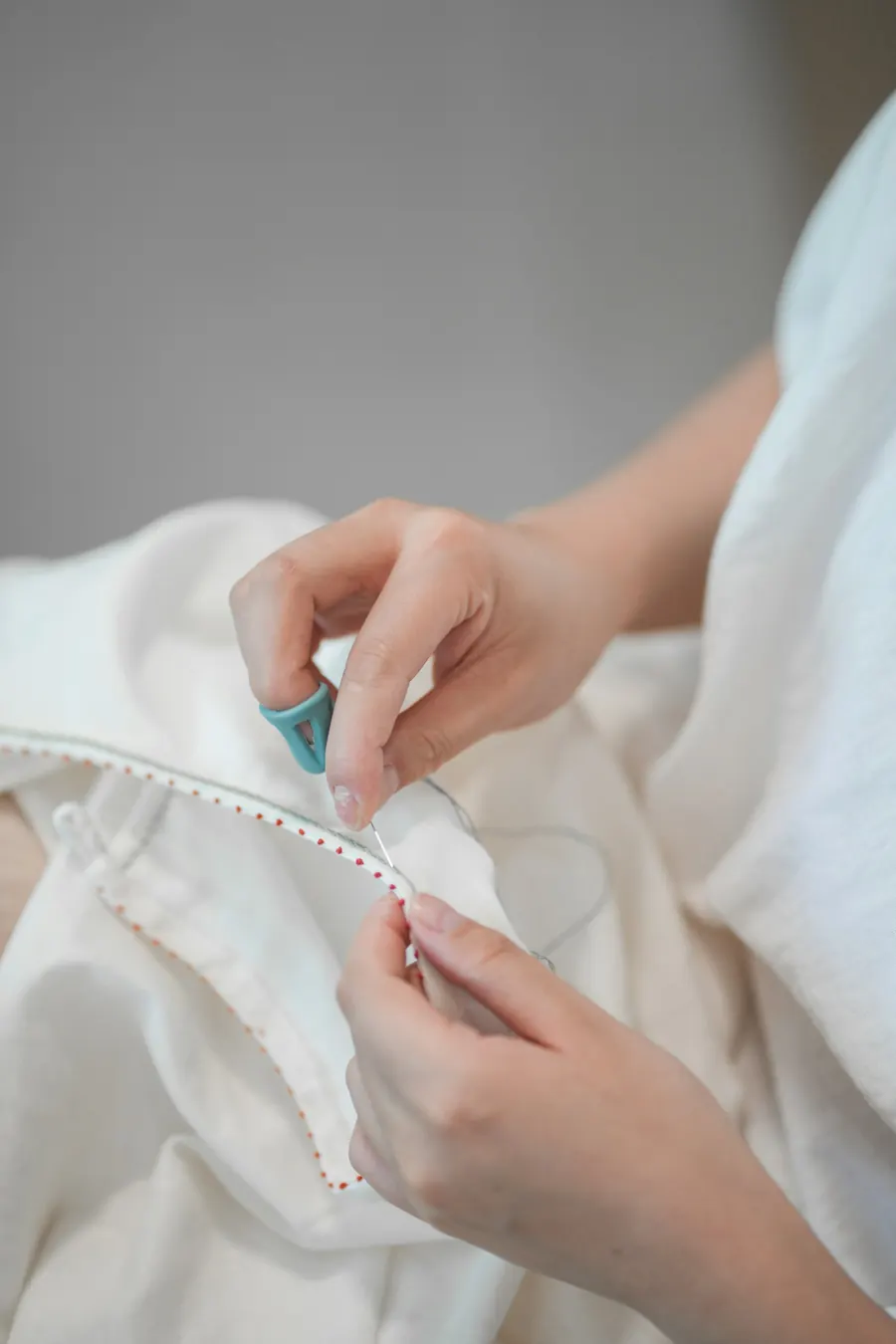 Mains de couturière qui cousent un tissu écru
