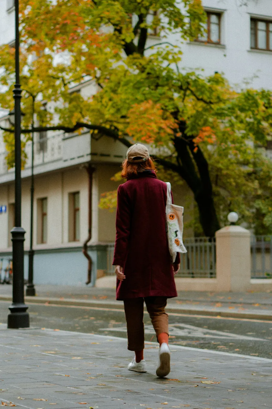 Femme de dos avec un manteau bordeaux dans une rue en automne