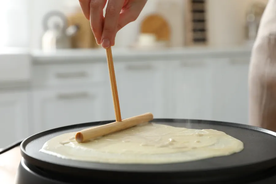 Mains qui étalent la pâte au rozell sur un billig en fonte, vapeur, gros plan