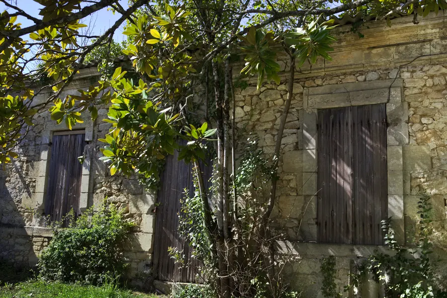 Maison en pierre de campagne aux volets fermés, jardin un peu laissé