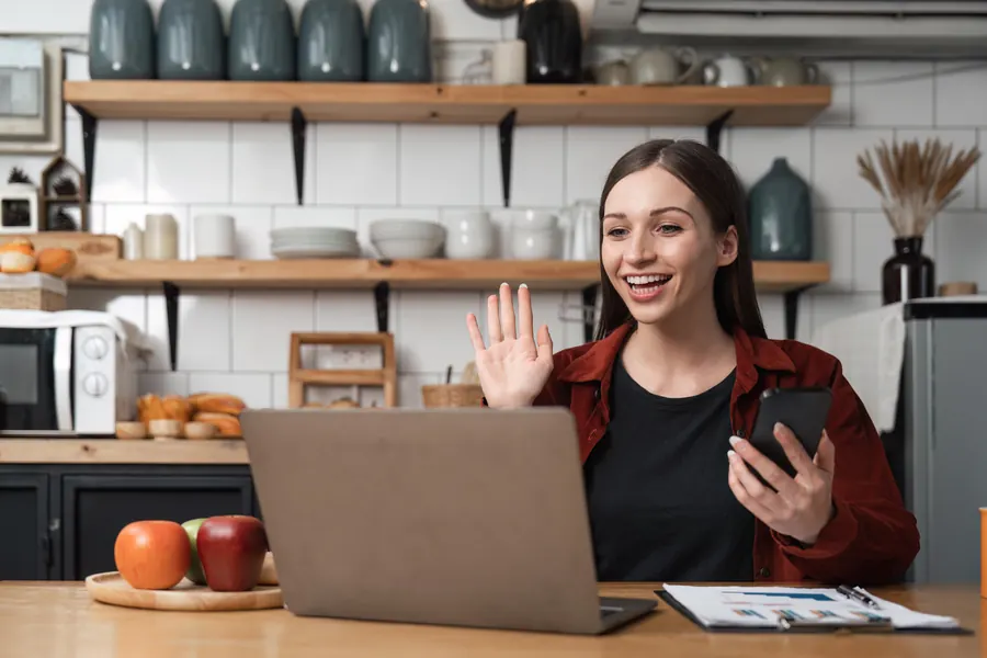 Femme en visio sur un ordinateur portable, à une table de cuisine en ville