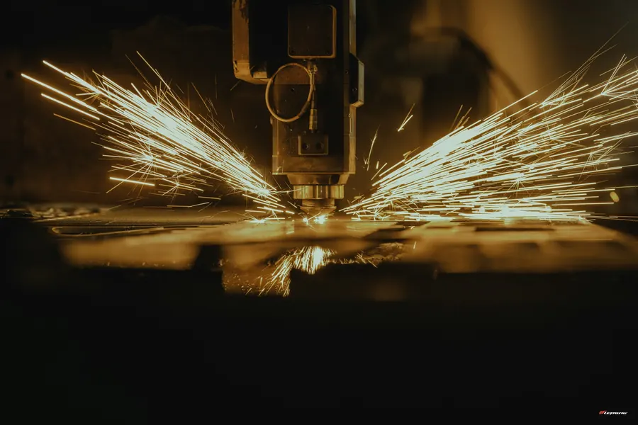Tête de découpe laser en action sur une tôle d'acier, gerbe d'étincelles, fond sombre