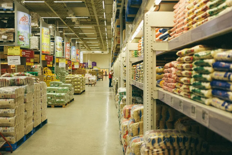 Allée d'un magasin-entrepôt avec palettes de sacs et rayonnages, lumière de hangar