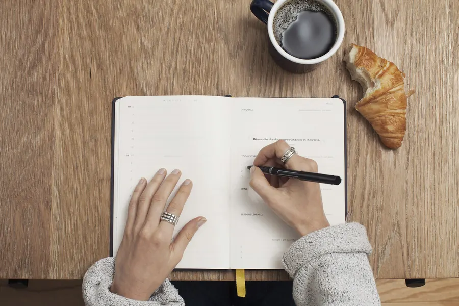 Main qui écrit dans un carnet à côté d'un café et d'un croissant