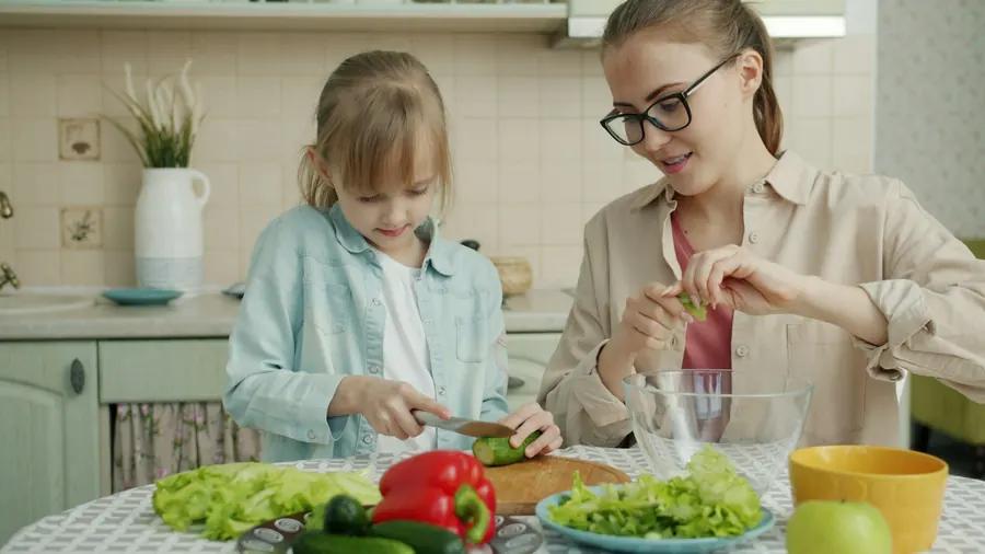 Mère et enfant qui coupent des légumes ensemble, cuisine familiale