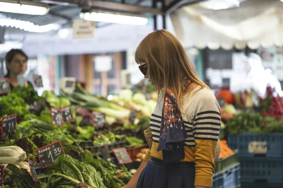 Femme qui choisit des légumes sur un marché de plein air, cageots et étal