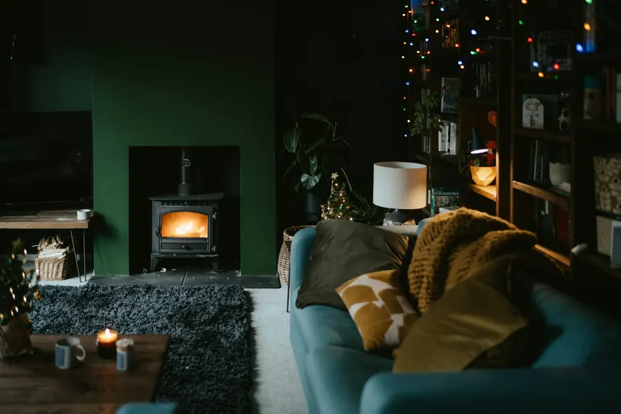 Séjour le soir éclairé par une lampe, des guirlandes et un poêle à bois allumé