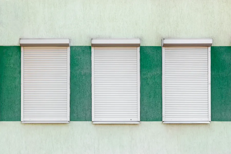 Trois volets roulants blancs fermés sur une façade, sans interrupteur visible