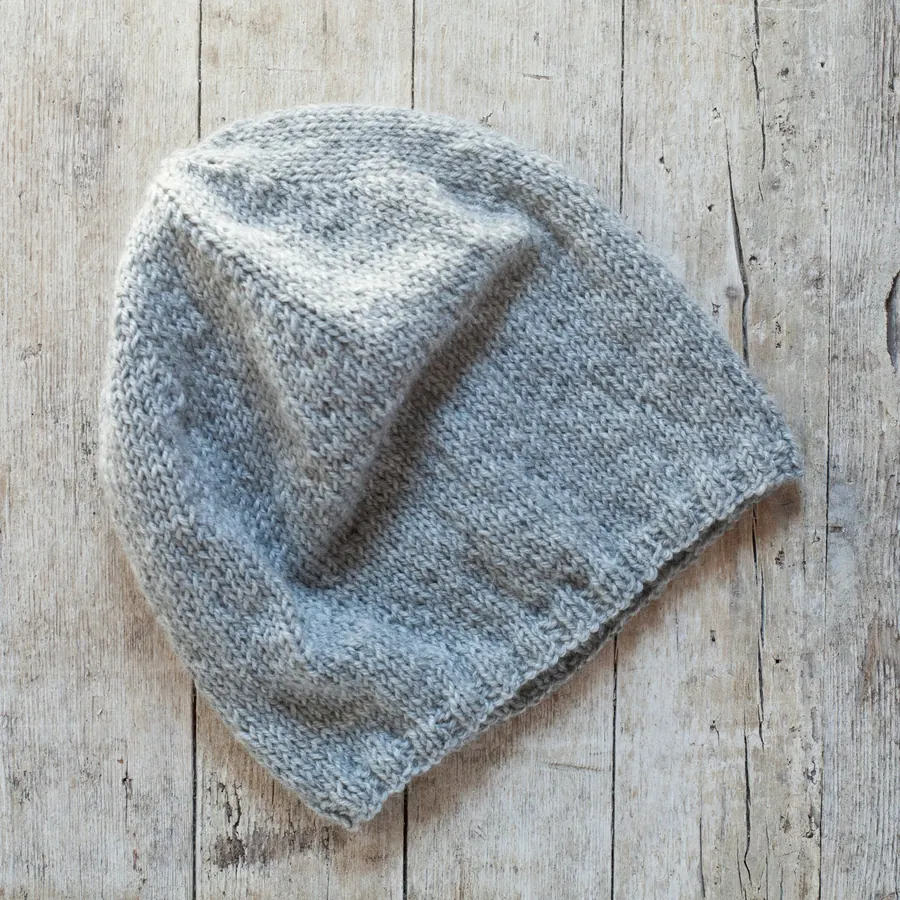 Bonnet tricoté main gris-bleu posé sur une table en bois