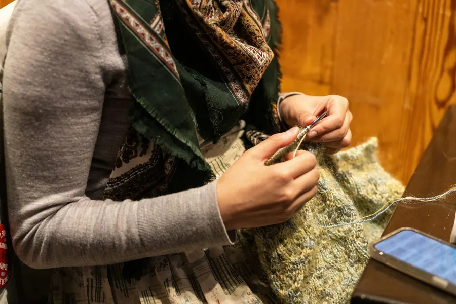 Femme qui tricote un vêtement kaki sur ses genoux