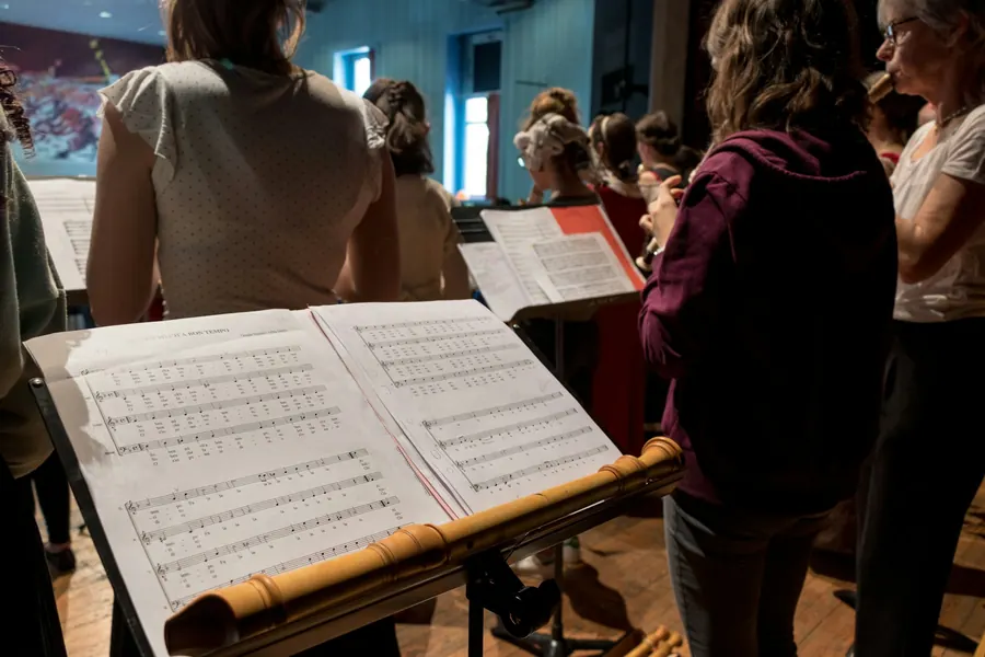 Chorale d'adultes de tous âges en répétition, partitions en main, cheffe de chœur de dos