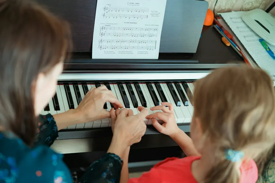 Une professeure aide une petite fille à jouer du piano