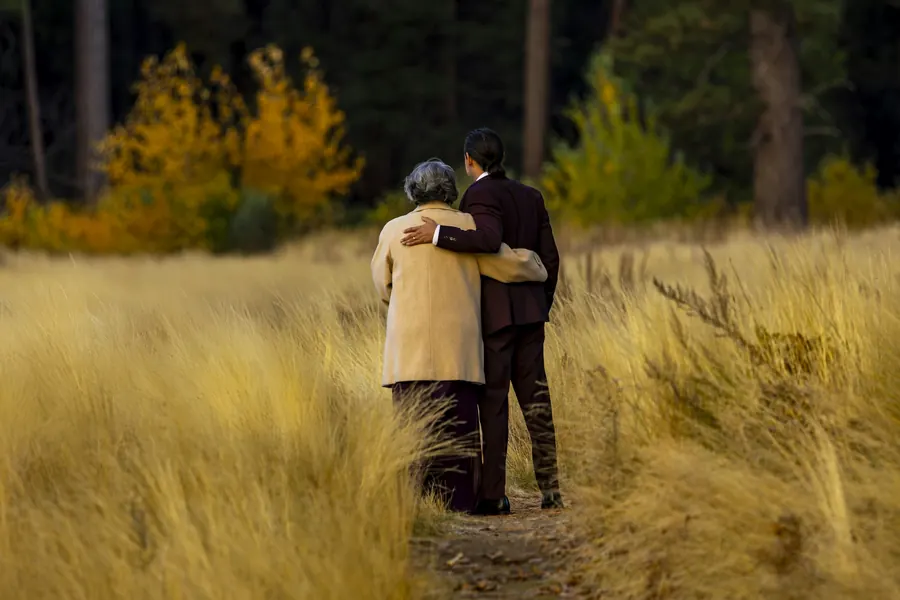 Dame âgée qui marche au bras d'un proche dans une prairie dorée d'automne