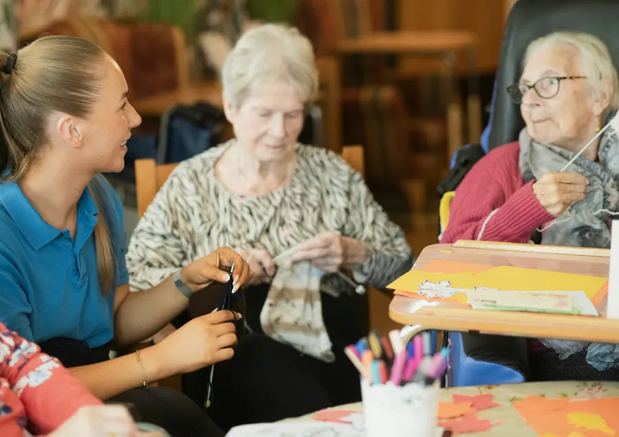 Une aide-soignante aide des résidentes autour d'une table d'activités