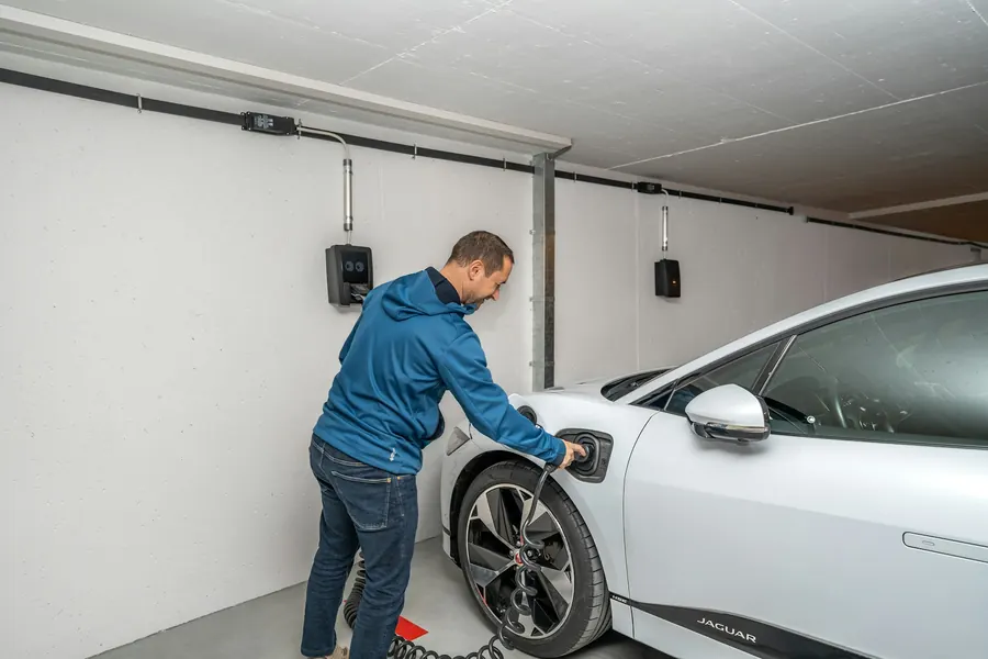 Électricien fixant une borne murale dans un garage, voiture électrique à côté