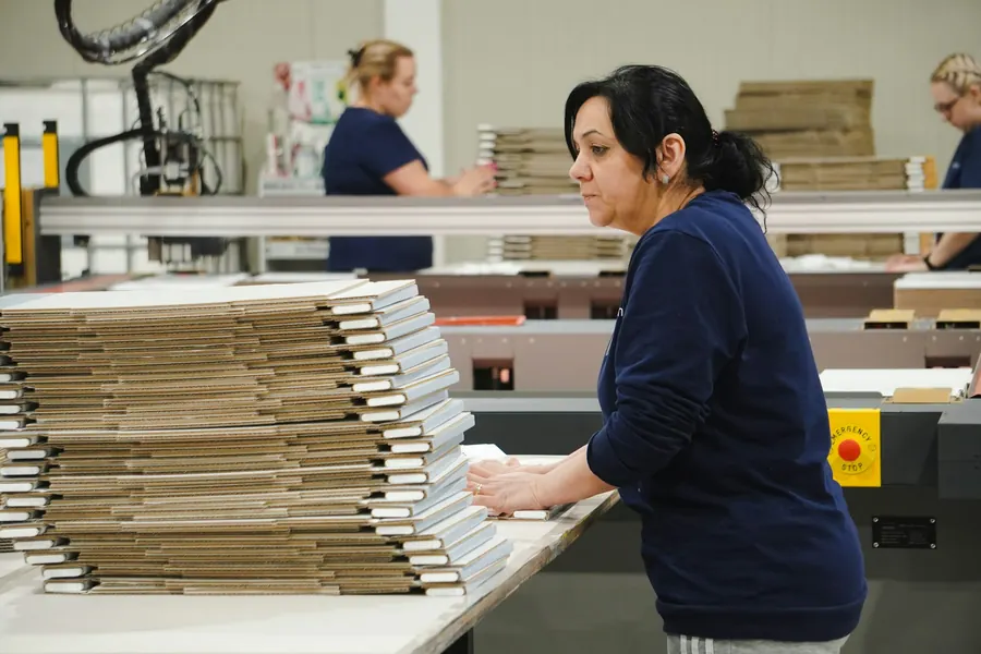Employée qui plie des cartons sur une table d'atelier