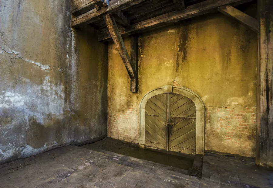 Porte en bois cintrée au fond d'une salle ancienne aux murs patinés, lumière chaude