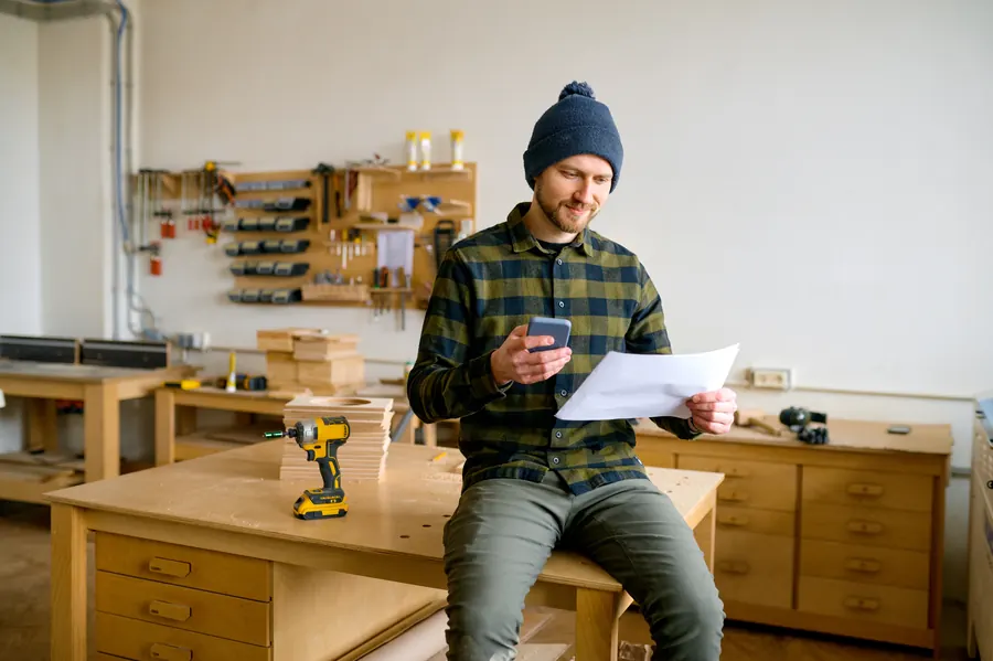 Menuisier photographiant une facture avec son téléphone dans son atelier