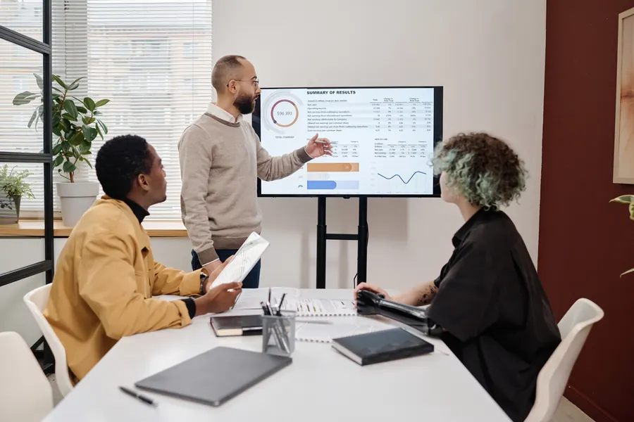 Dirigeant de PME et deux salariés autour d'une table, tableau de bord sur écran