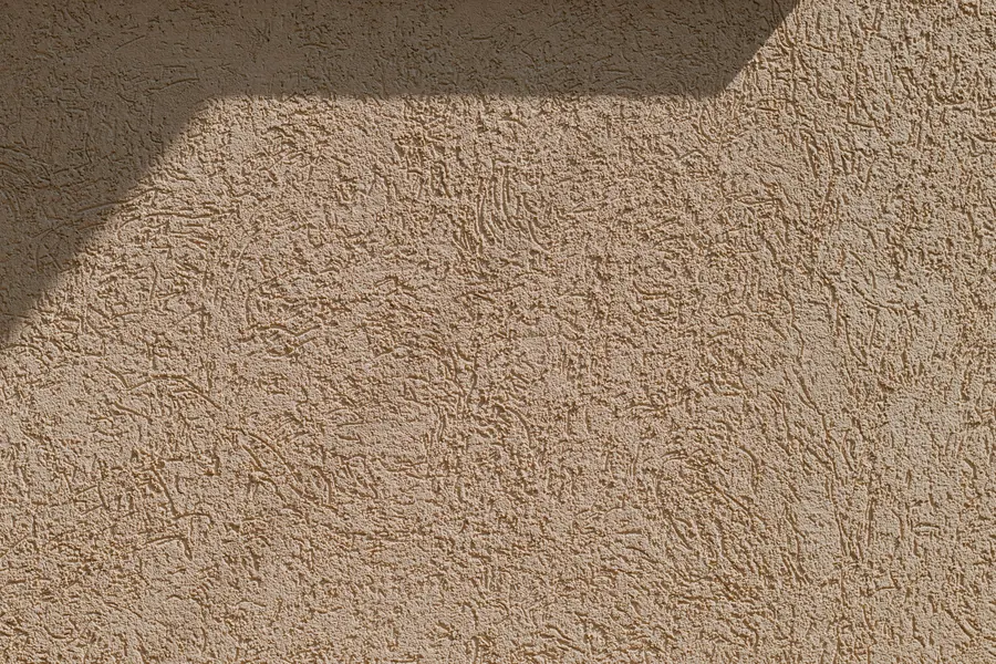 Gros plan d'une finition d'enduit grattée, grain régulier, lumière rasante