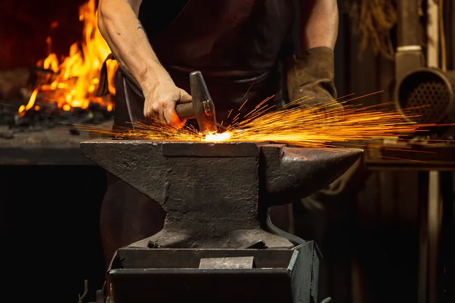 Forgeron qui frappe un fer rougi sur l'enclume, étincelles, atelier sombre