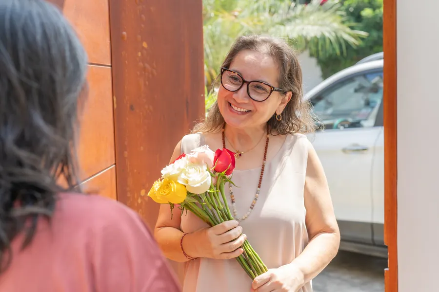 Livreur qui tend un bouquet emballé devant une porte de maison en pierre