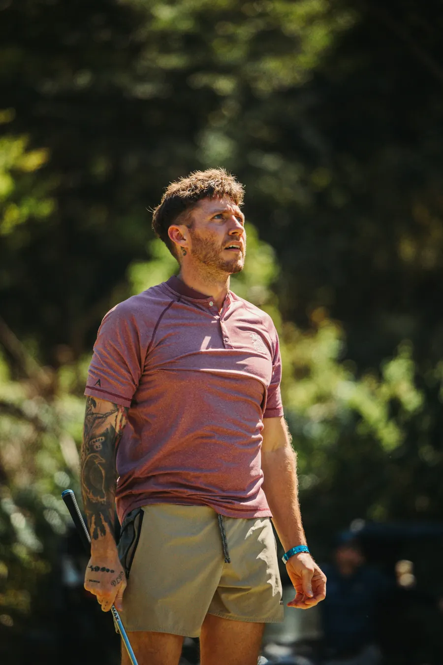 Golfeur tatoué en polo rose qui regarde le ciel