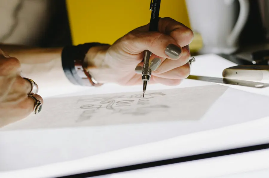 Main qui trace un lettrage au crayon sur du papier calque