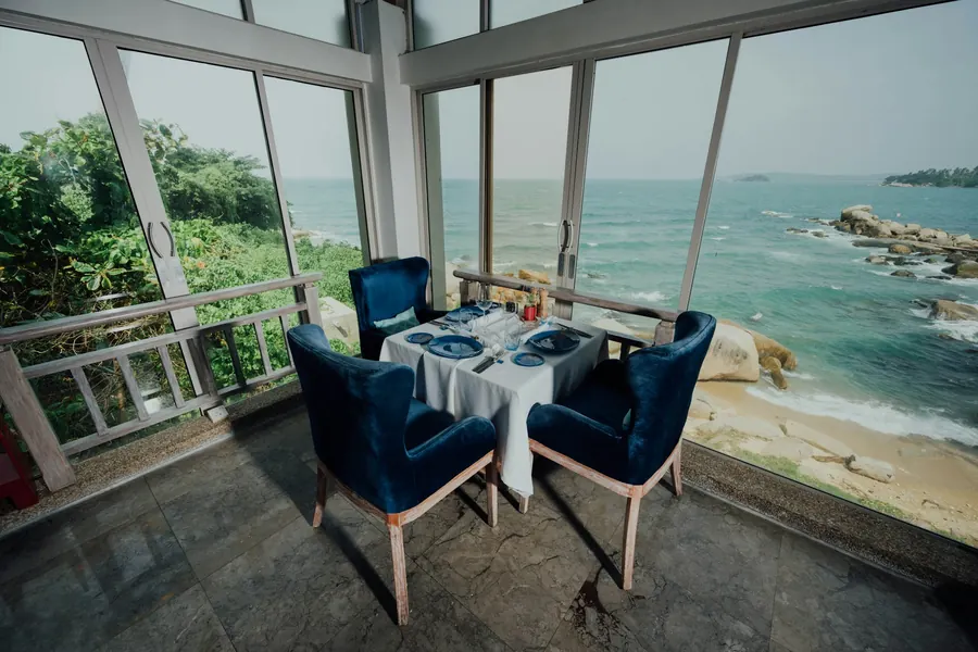 Table dressée avec chaises bleues, devant une baie vitrée sur la mer