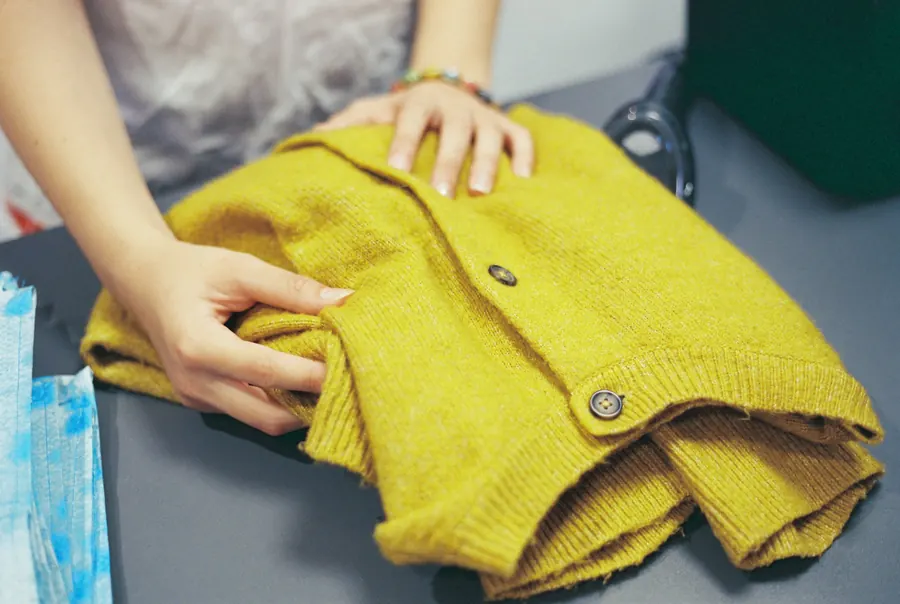 Mains qui plient un vêtement en laine jaune sur une table