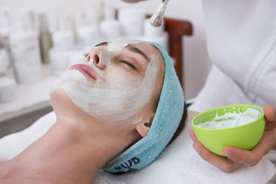 Soin du visage en cours, cliente allongée de profil, mains de l'esthéticienne, lumière douce