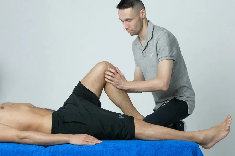 Kiné qui guide un patient dans un exercice de flexion du genou sur une table, cicatrice discrète