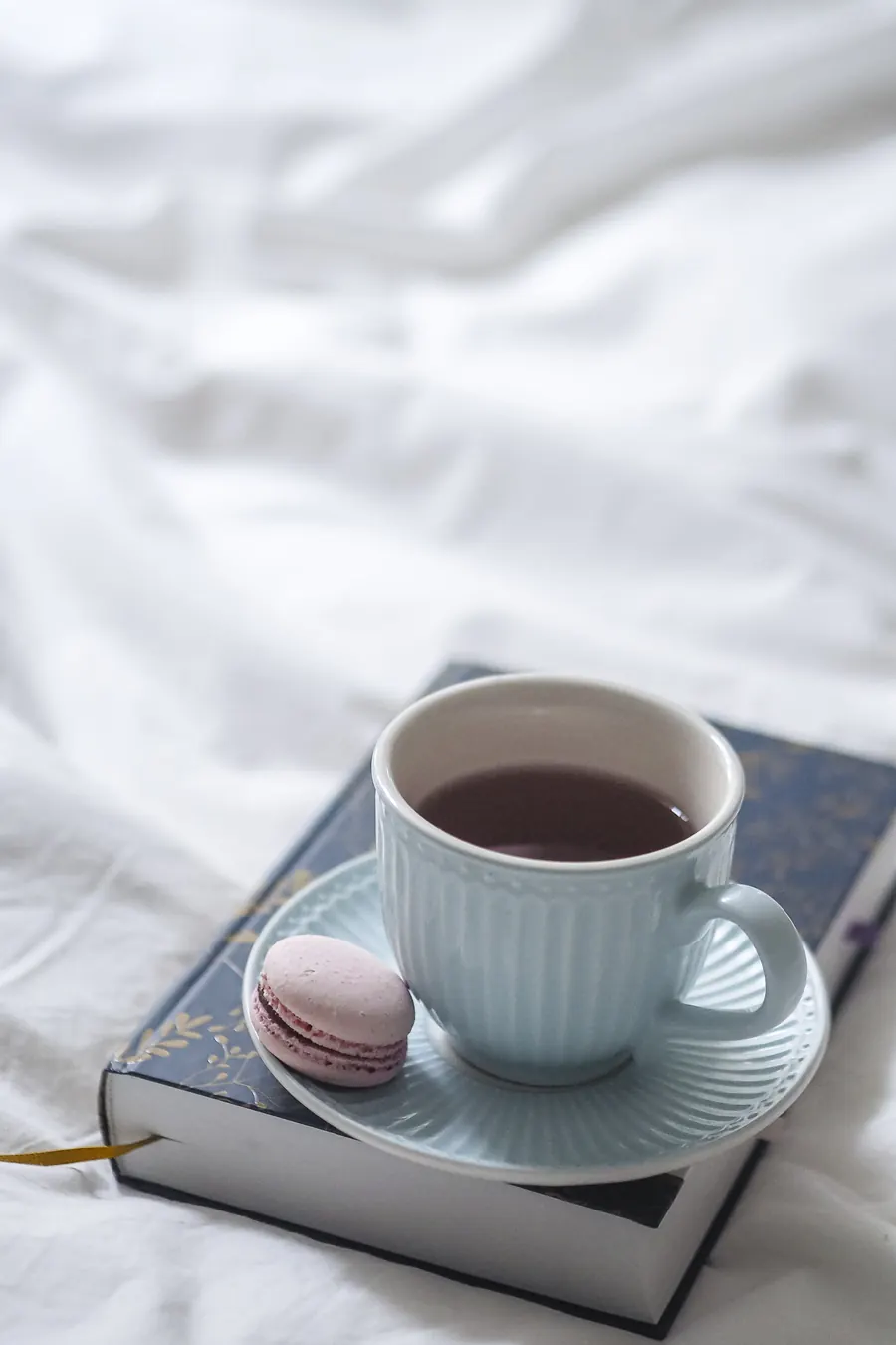 Roman grand format posé sur une nappe en lin, tasse de thé, couverture sans texte lisible