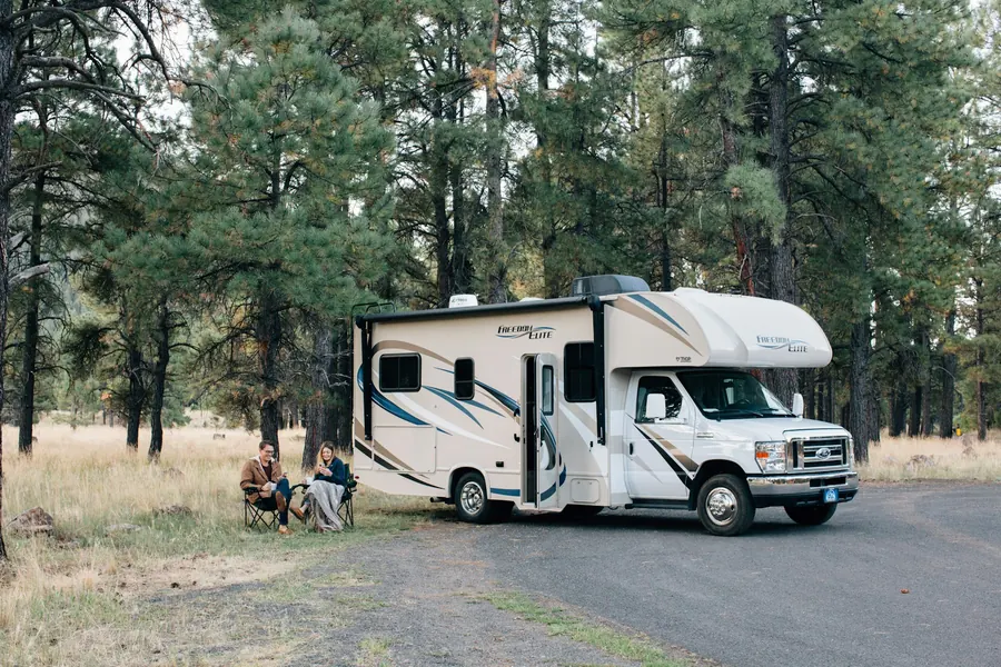 Camping-car capucine avec lit au-dessus de la cabine, famille qui installe la table devant