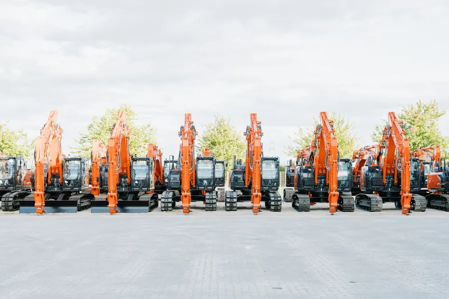 Rangée de mini-pelles orange alignées sur le parking d'un dépôt