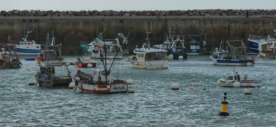 Bateaux de pêche amarrés dans un port abrité par une digue, ciel gris