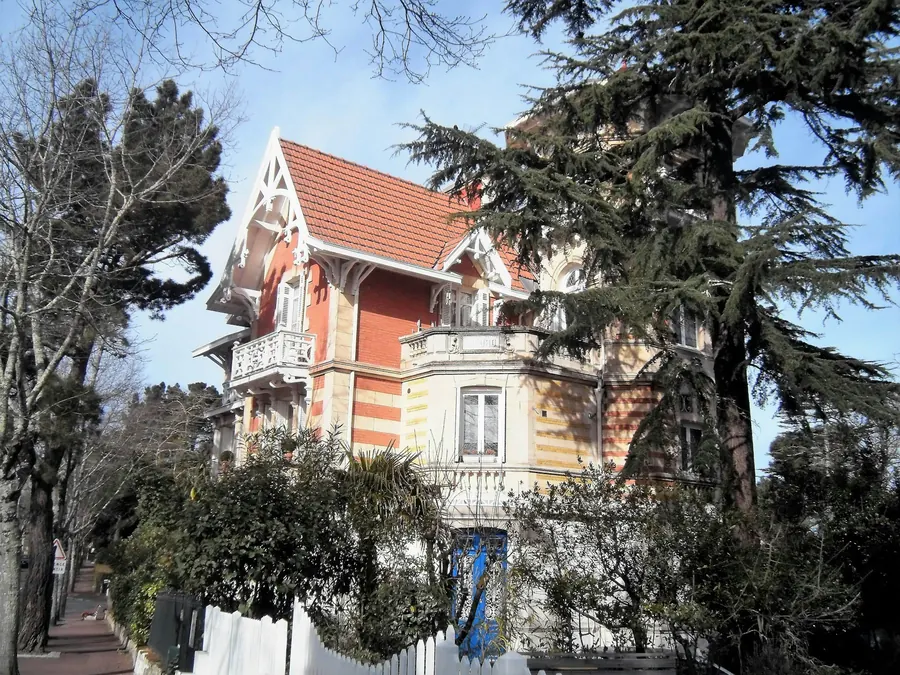 Villa ancienne aux boiseries décoratives et toit pentu, entourée d'arbres, sans famille visible