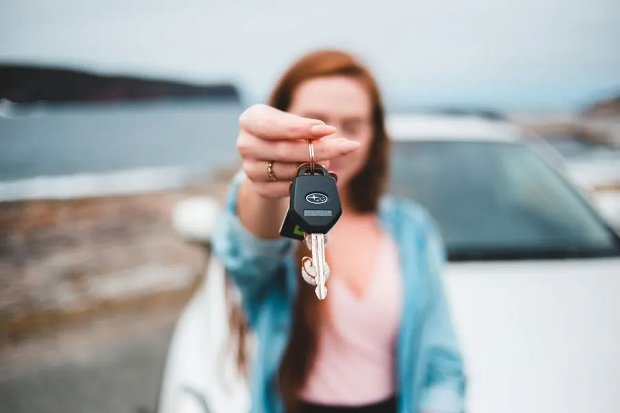 Jeune femme qui tend une clé de voiture devant une berline blanche