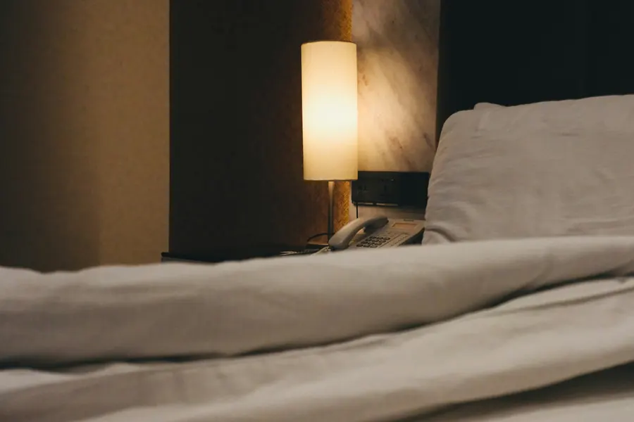 Détail de linge de lit blanc et d'une lampe de chevet, grain de la matière, ambiance feutrée