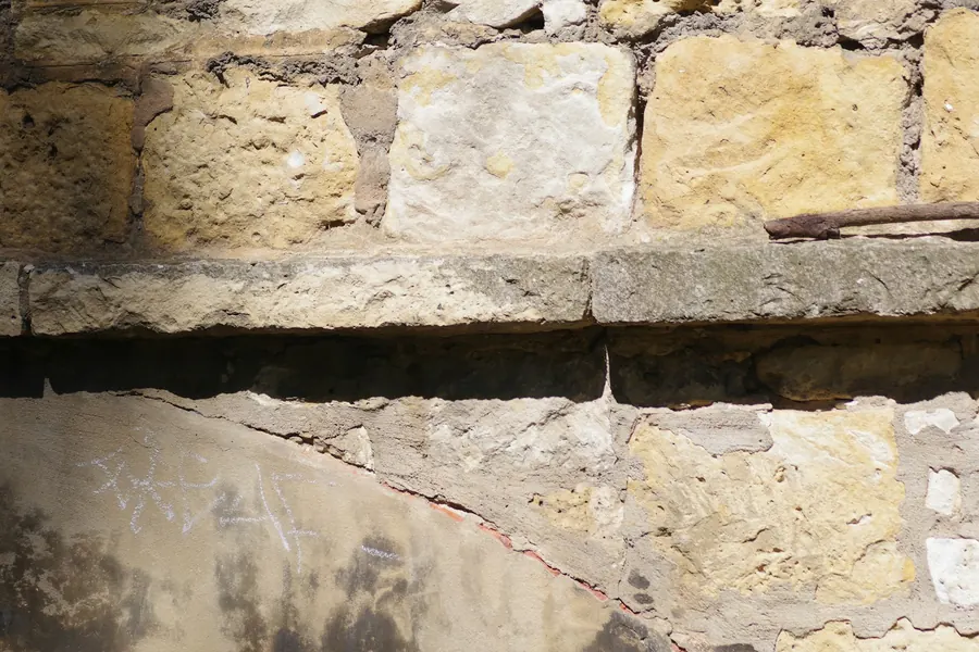 Maçon qui rejointoie un mur de pierre à la chaux, gros plan sur la truelle langue de chat et les joints clairs