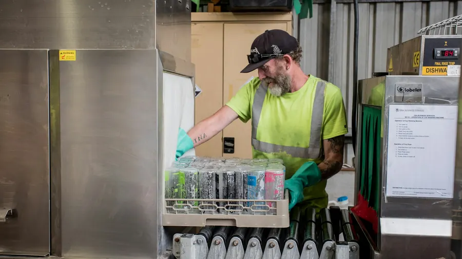 Ouvrier qui charge un casier de verres dans un lave-vaisselle à capot