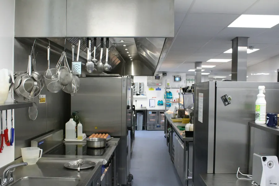 Cuisine professionnelle en inox avec ustensiles suspendus, sans batteur ni coupe-légumes visibles